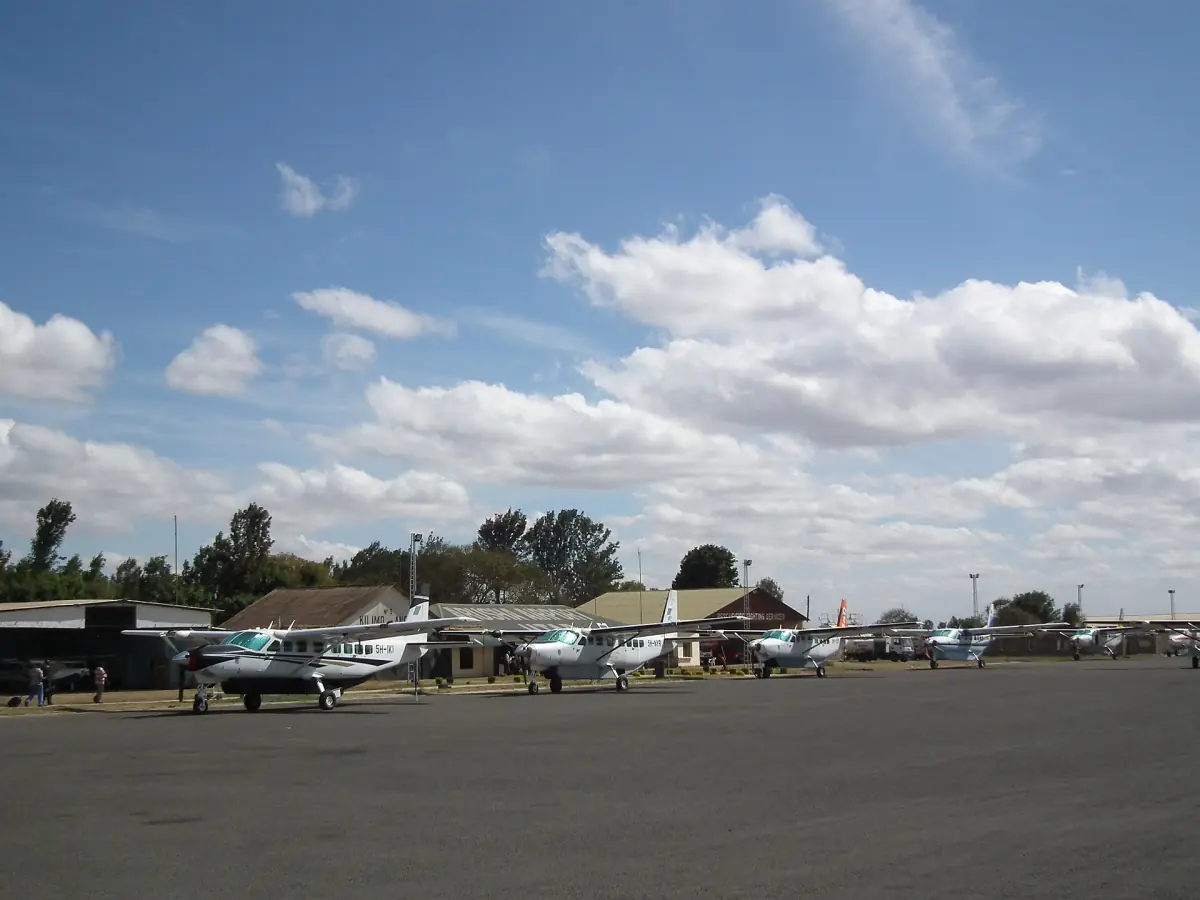 Kleine vliegtuigen op een rij op Arusha Airport onder een gedeeltelijk bewolkte lucht
