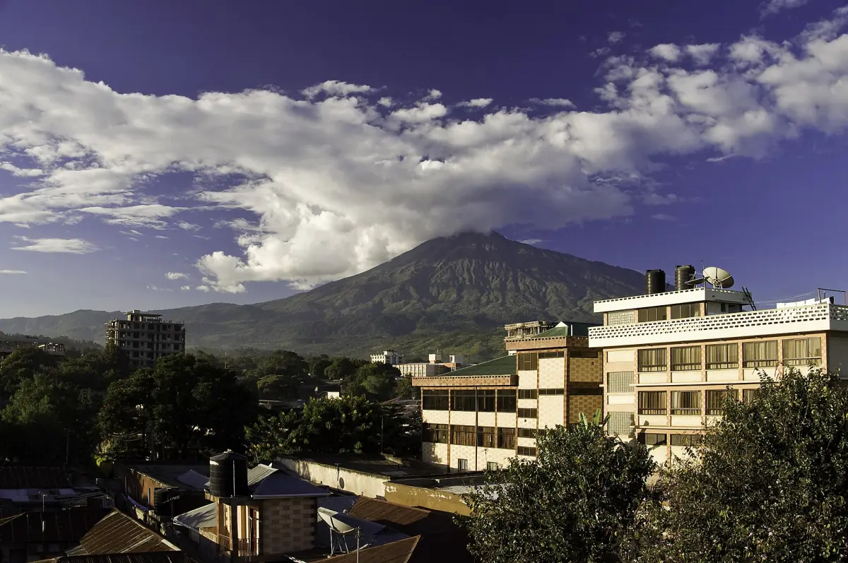 Der Mount Meru erhebt sich hinter den Gebäuden und Bäumen von Arusha