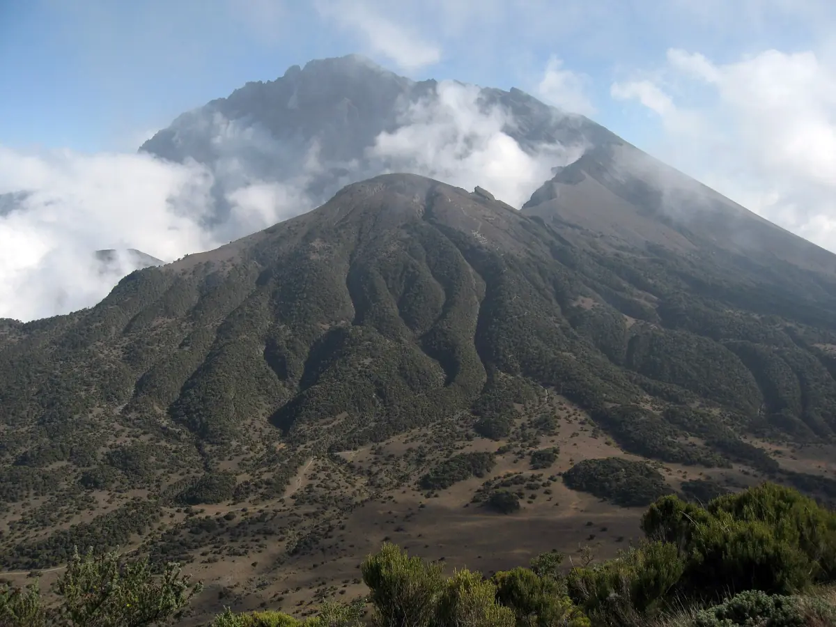 Kraterwand und Ascheskegel des Mount Meru mit Wolken über dem Grat